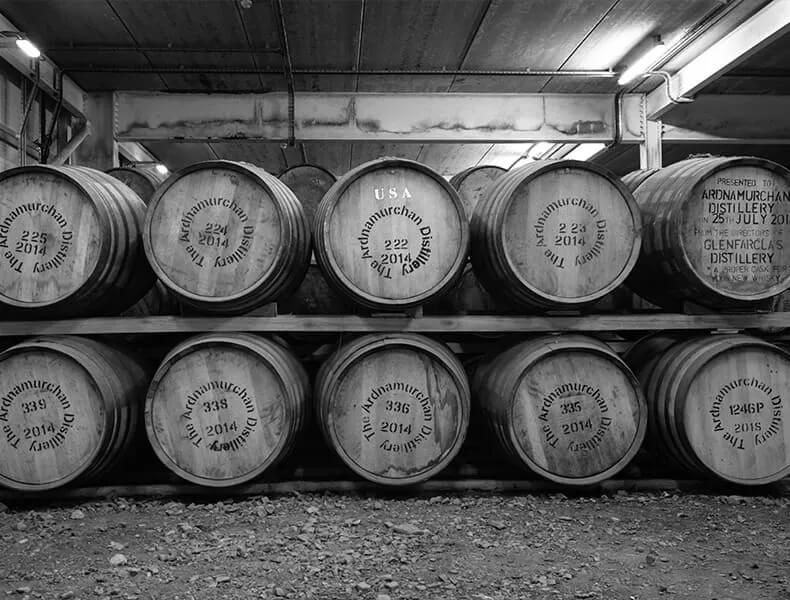 Ein Stapel Holzfässer mit der Aufschrift Ardnamurchan Distillery und den Jahreszahlen, gelagert in einem schwach beleuchteten Lagerhaus der Brennerei.