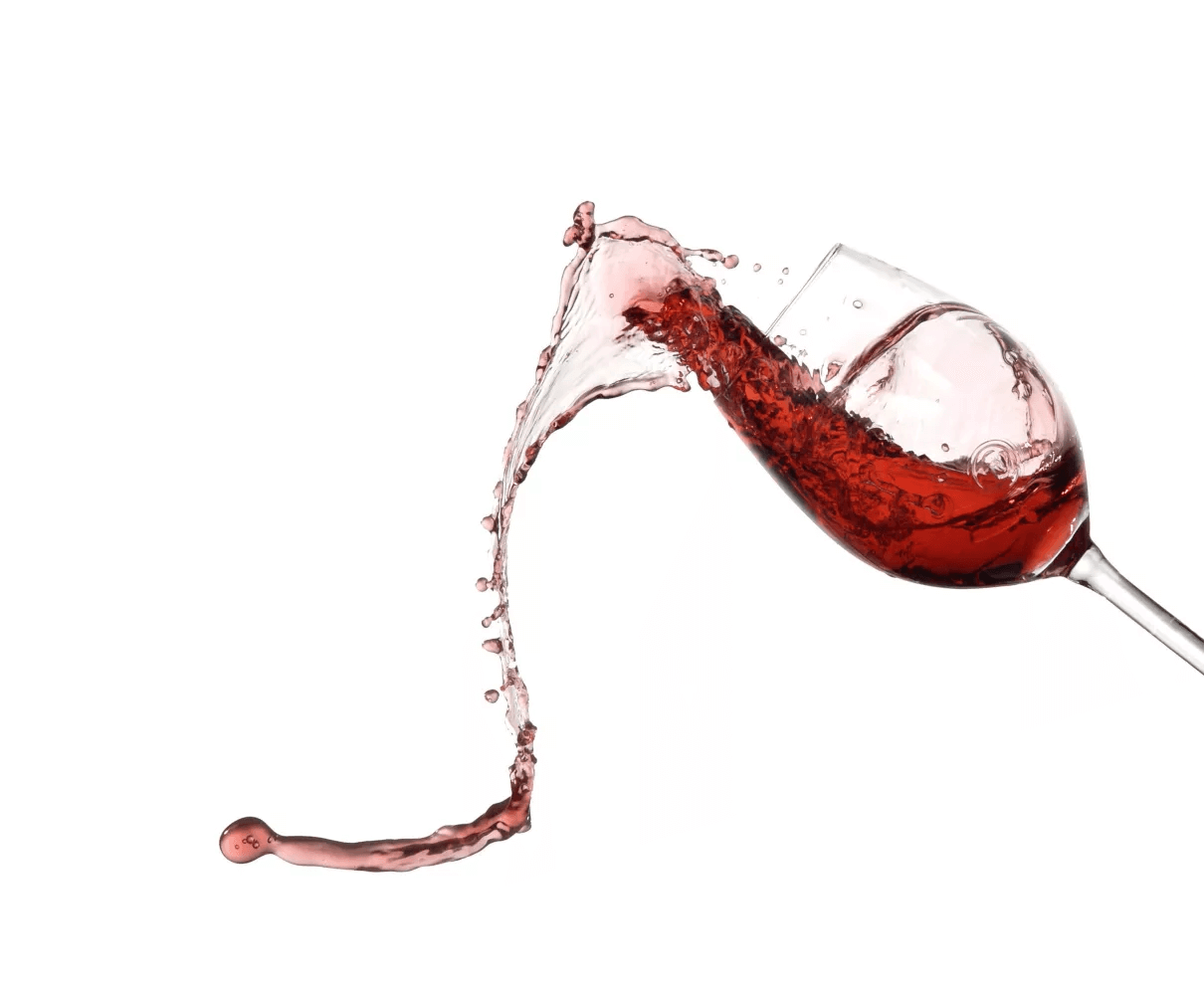 Ein dynamischer Spritzer Rotwein ergießt sich aus einem gekippten Glas und bildet Tröpfchen vor einem weißen Hintergrund.